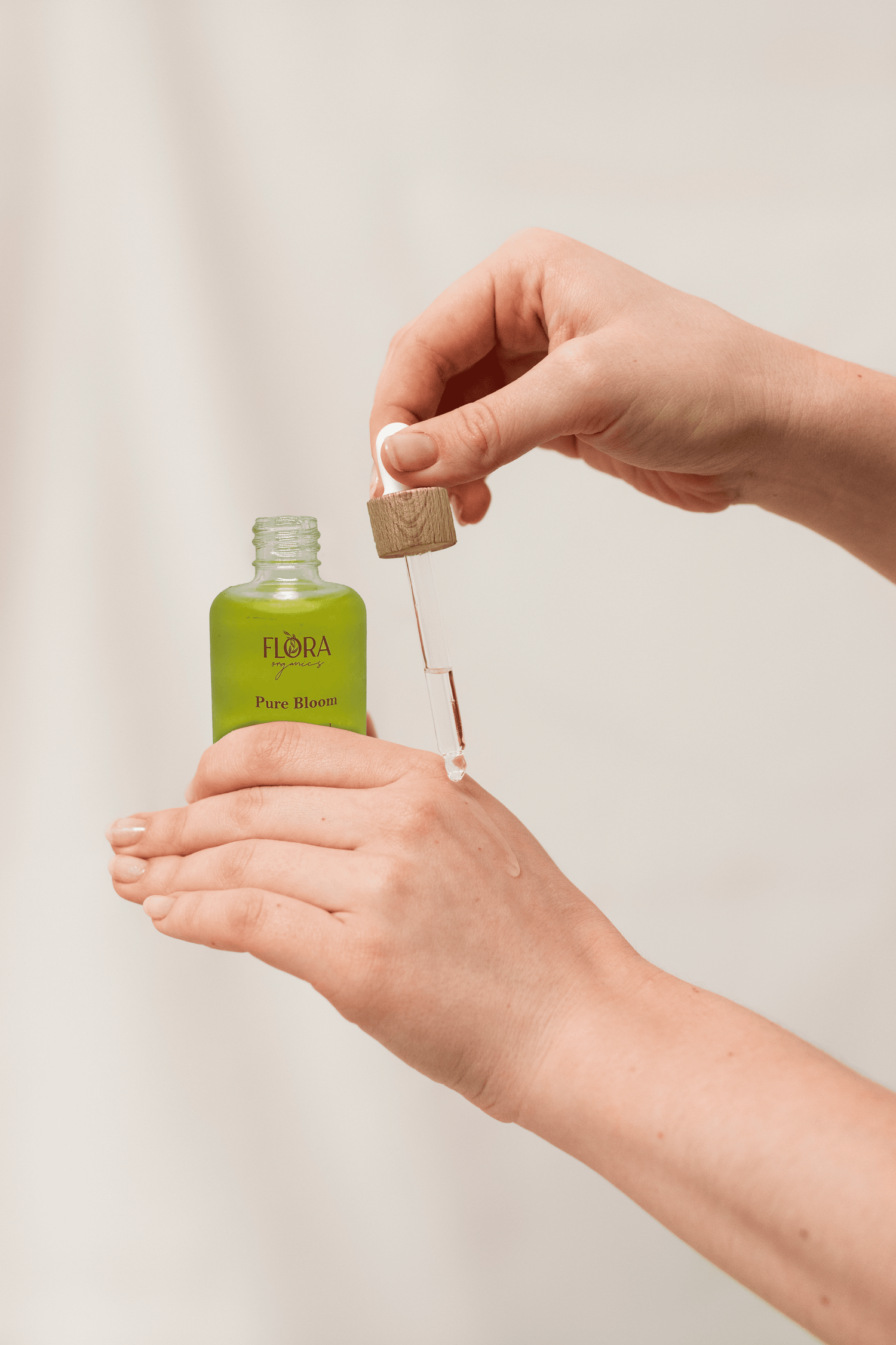 Hands holding Flora Organics Pure Bloom Oil and dropper, applying product on back of hand