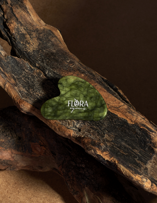 Flora Organics jade gua sha stone resting in a tree bark.