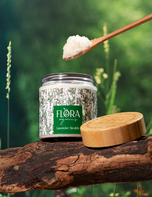 Lavender body scrub from Flora Organics in open jar on tree bark, with wooden lid and spoonful of scrub held above