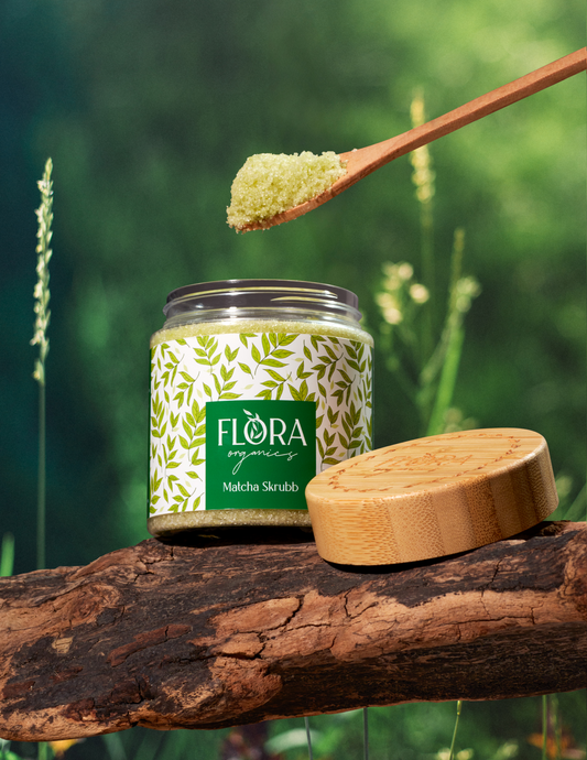 Matcha body scrub from Flora Organics in open jar on tree bark, with wooden lid and spoonful of scrub held above