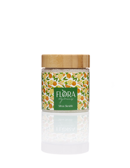Flora Organics Citrus Scrub in glass jar with bamboo lid, reflected on white background
