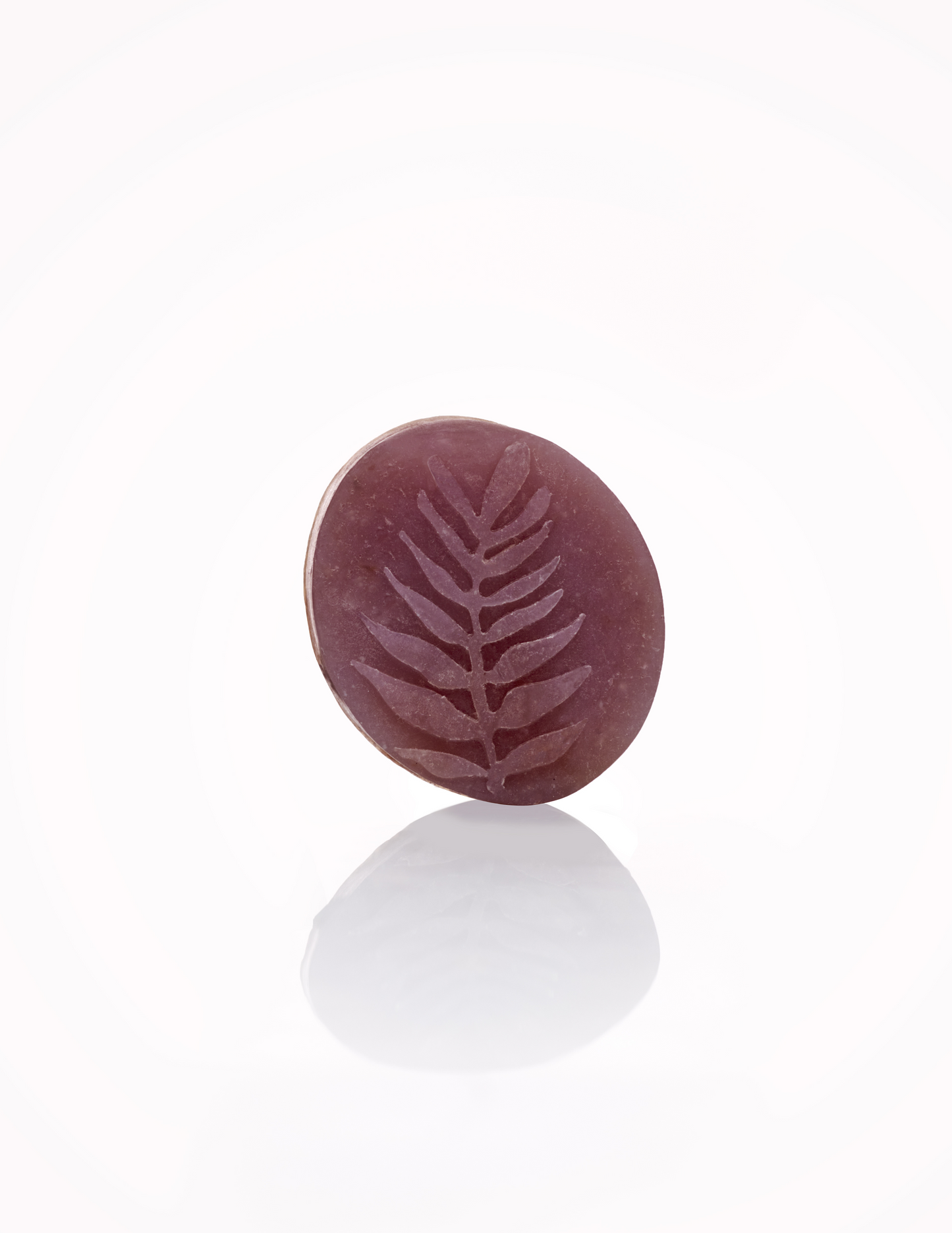 Flora Organics round lavender soap bar with fern imprint, reflected on white background