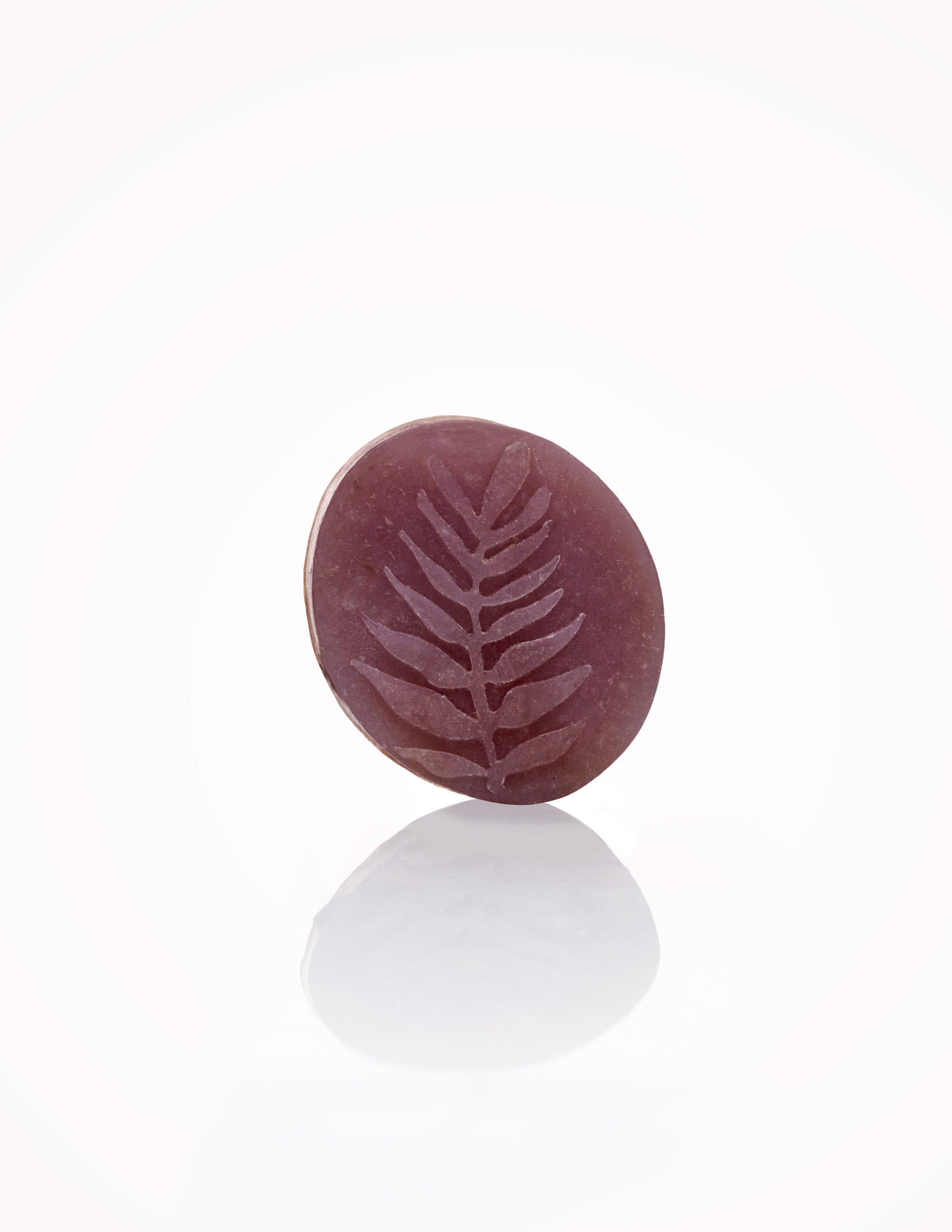 Flora Organics round lavender soap bar with fern imprint, reflected on white background