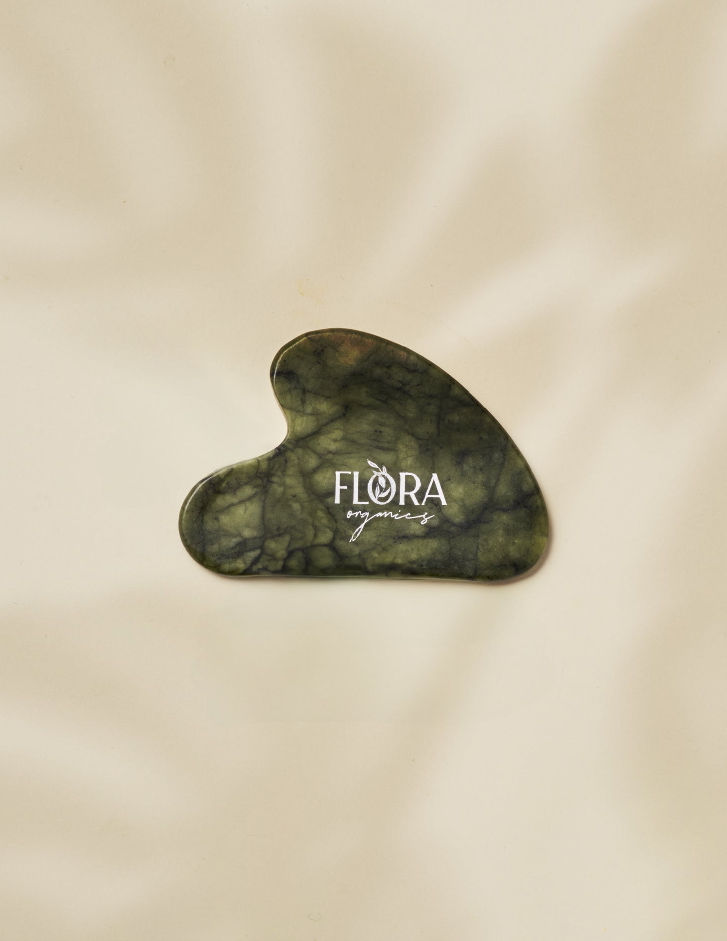 Flora Organics jade gua sha stone on soft beige fabric background