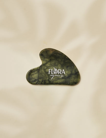 Flora Organics jade gua sha stone on soft beige fabric background