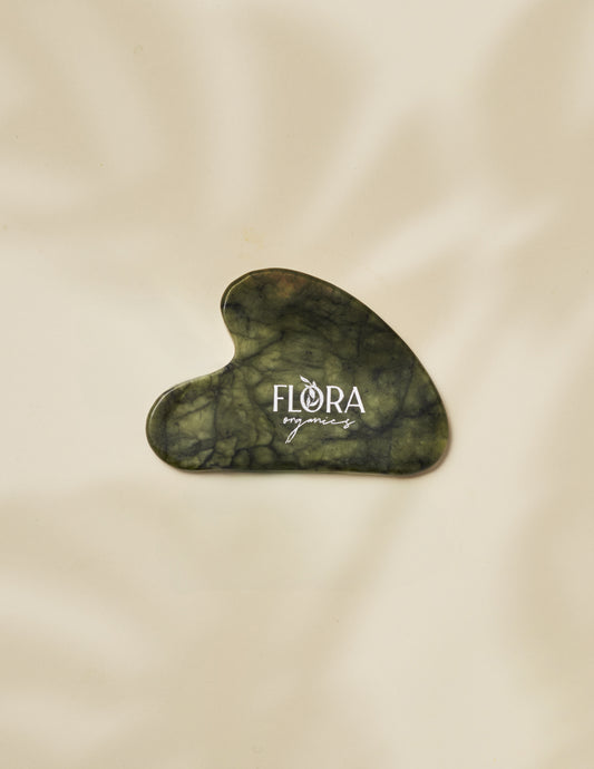 Flora Organics jade gua sha stone on soft beige fabric background